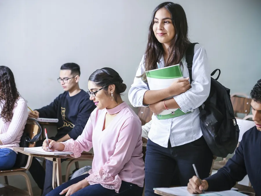 Estudiantes en una sala de clases; una de ellas sonríe con sus apuntes