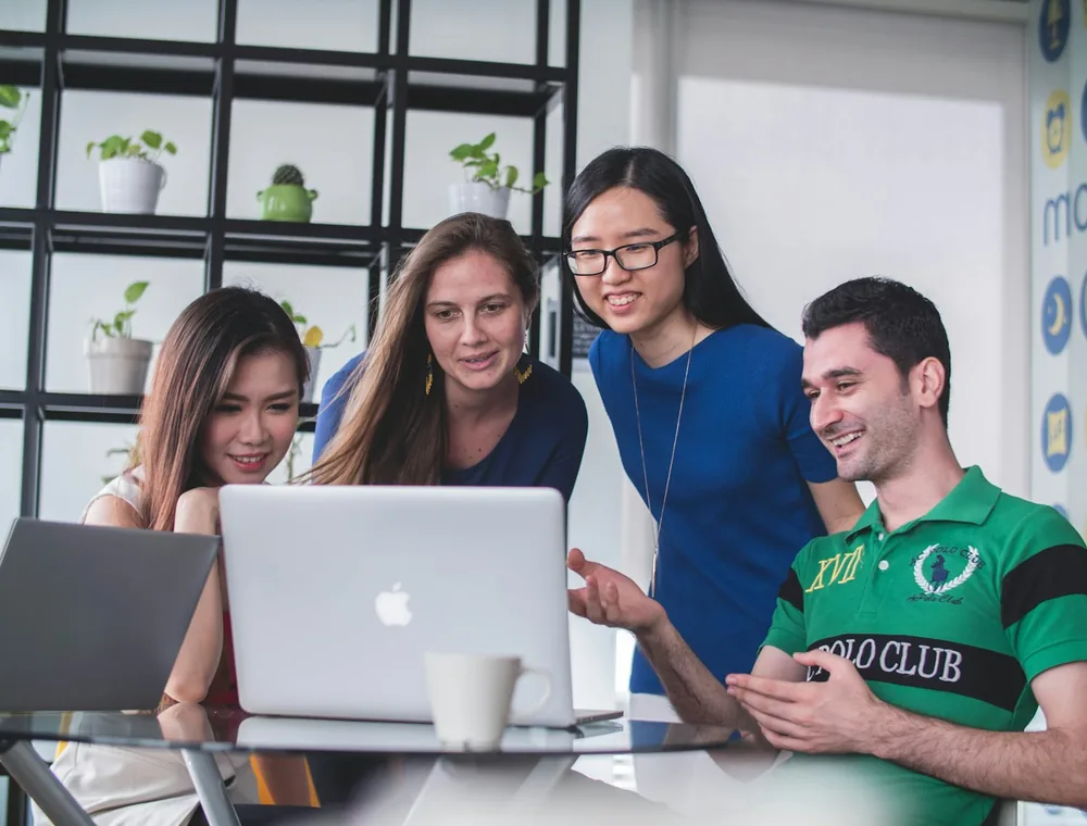 Cuatro personas de un equipo sonríen mientras revisan juntas un curso en un computador portátil